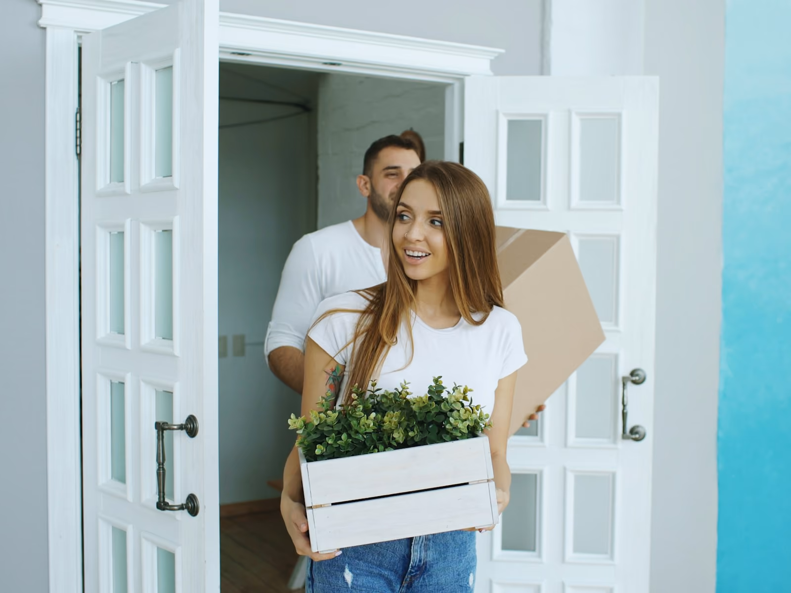 Dos personas entrando a su nuevo cuarto con una caja y una planta